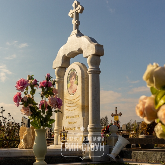 Памятник женщине из мрамора в виде арки, котору венчает православный крест. Ваза и столбики ограды также выполнены из мрамора.