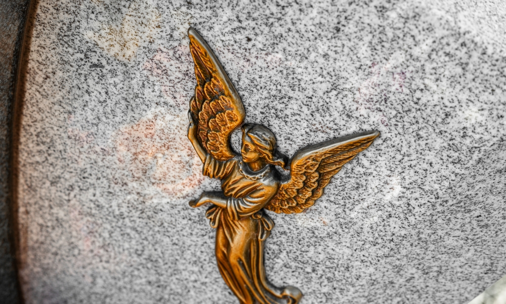 Бронзовый барельеф в виде ангела с крыльями на сером граните